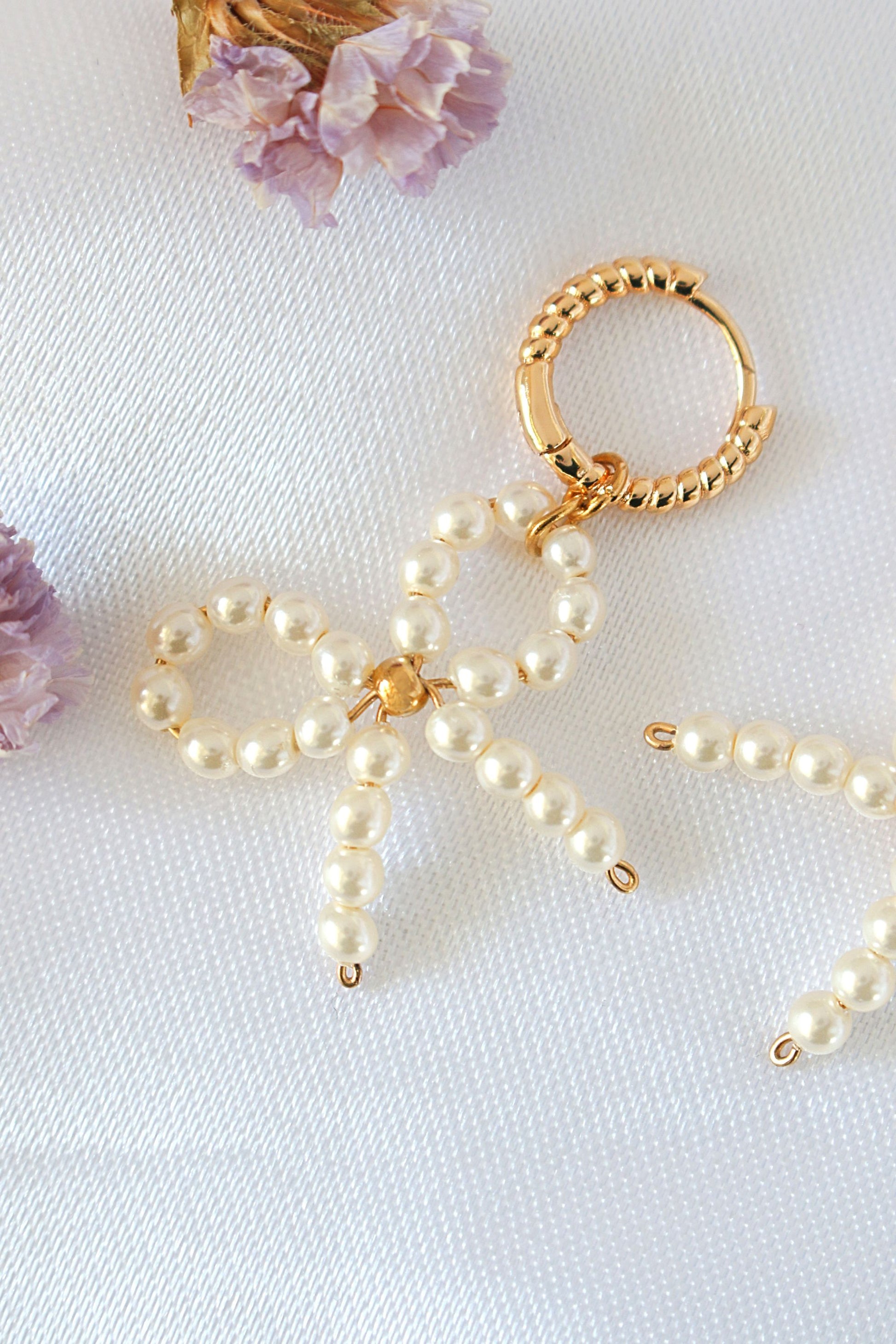 Pearl bow keychain on a white surface with purple flowers