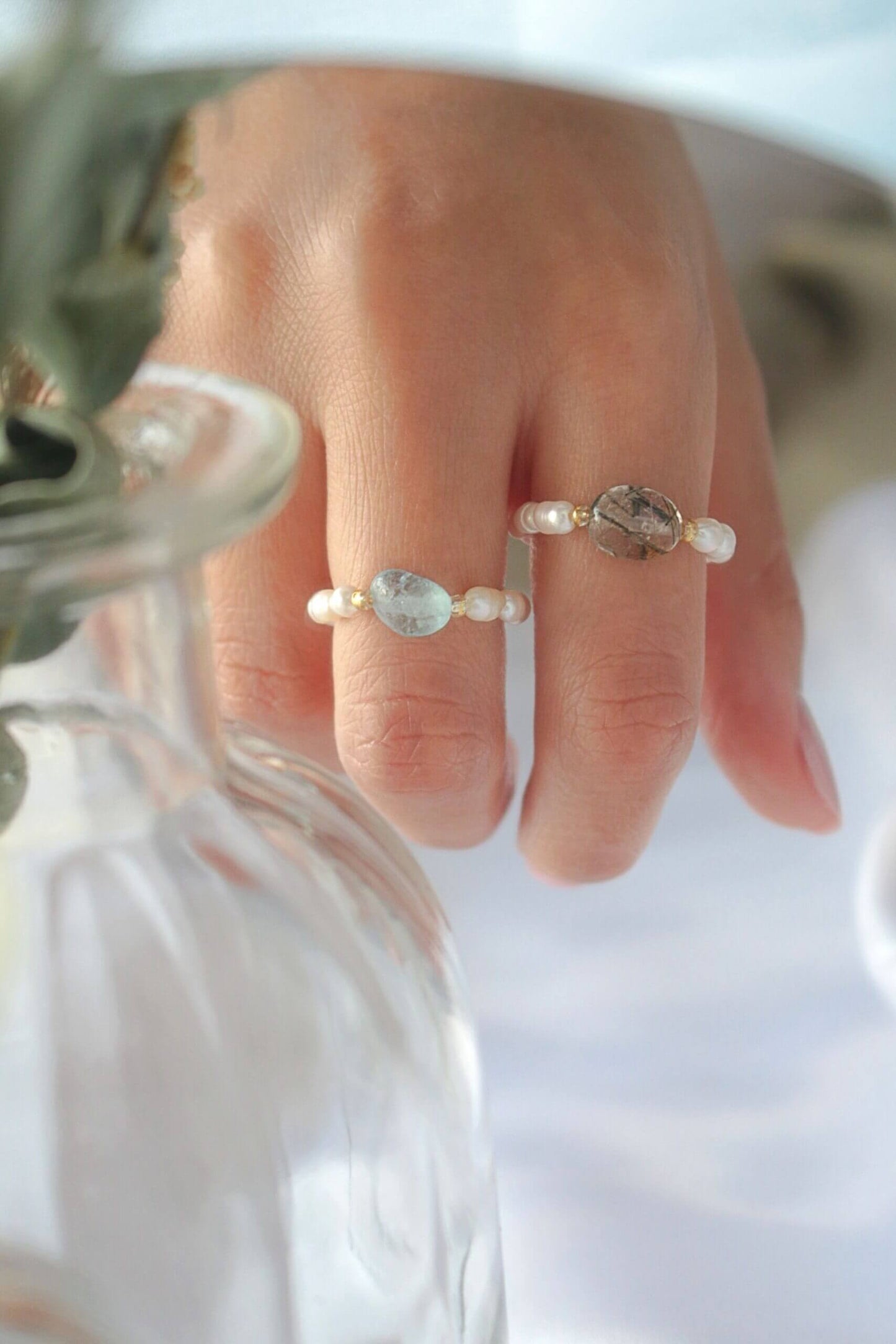 Close-up of a hand wearing two pearl rings with a blurred background