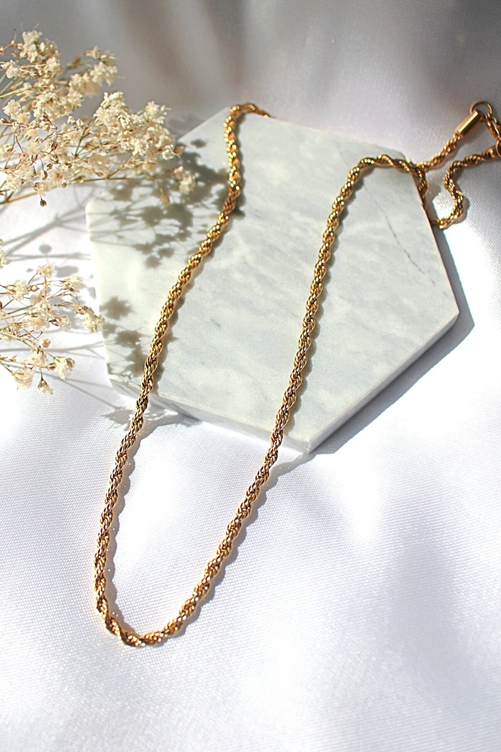 Gold chain necklace on a white surface with dried flowers