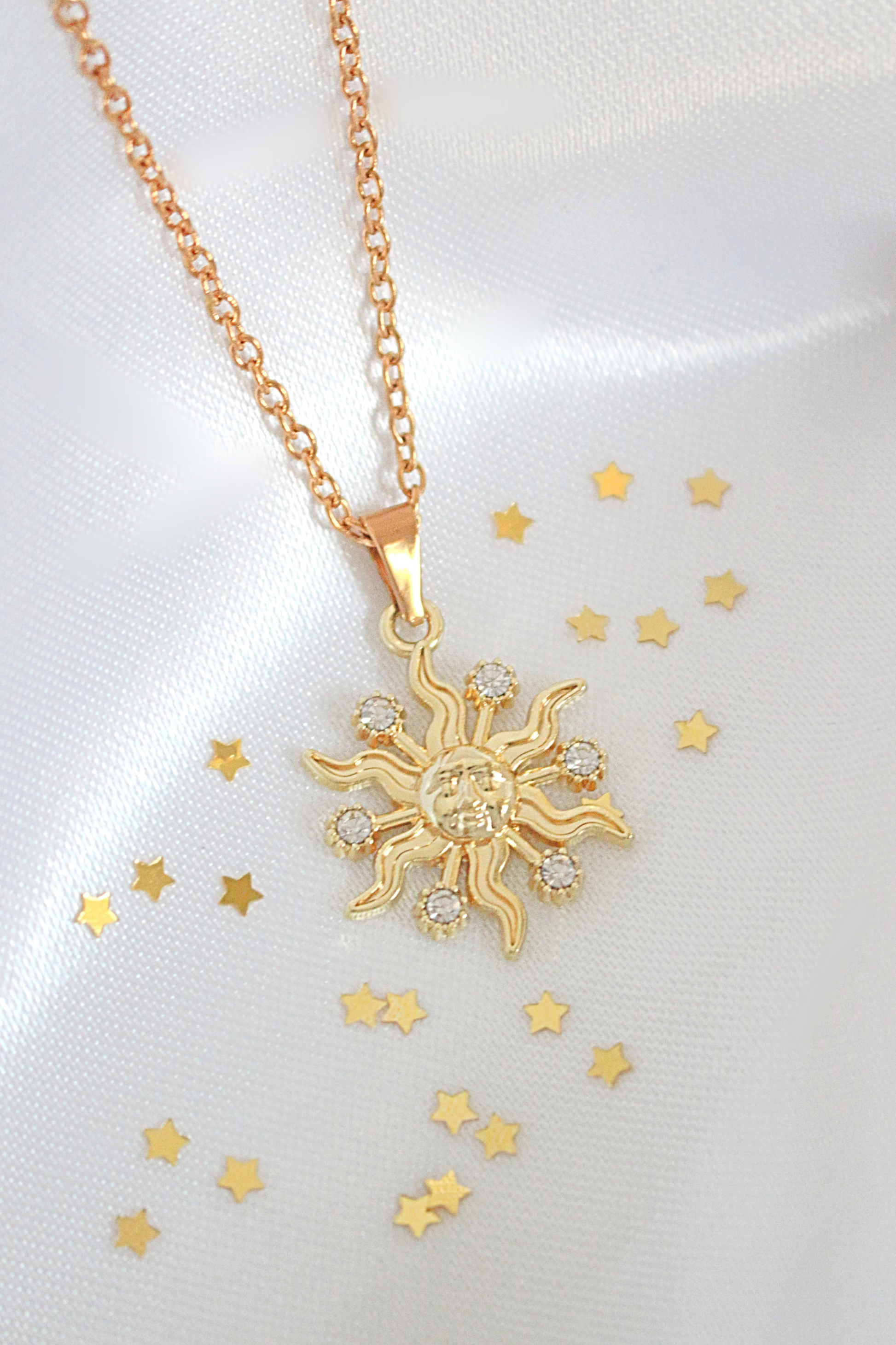 Gold sun-shaped pendant necklace on a white background with gold stars