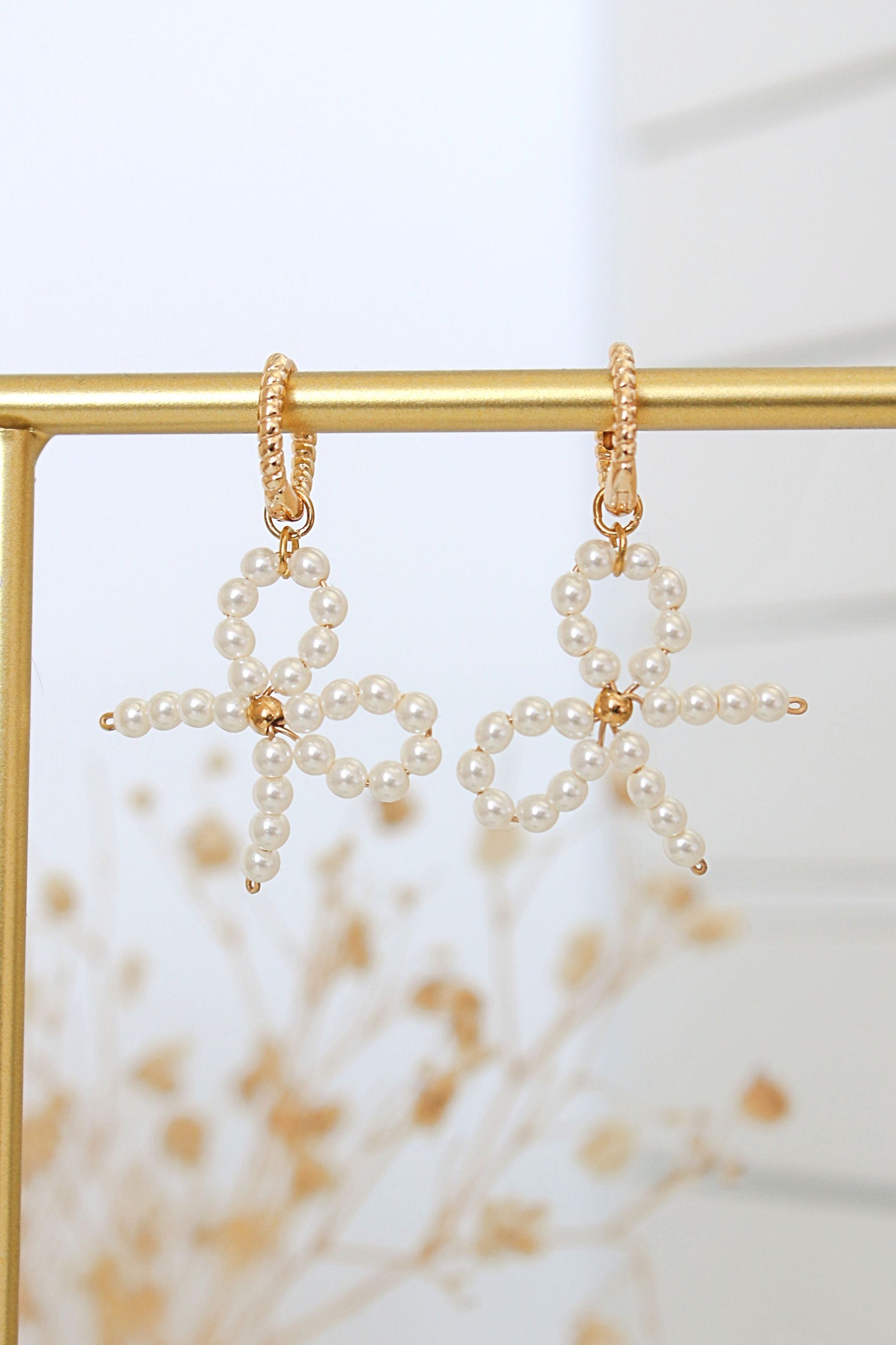 Pearl star-shaped earrings on a gold stand with a blurred natural background