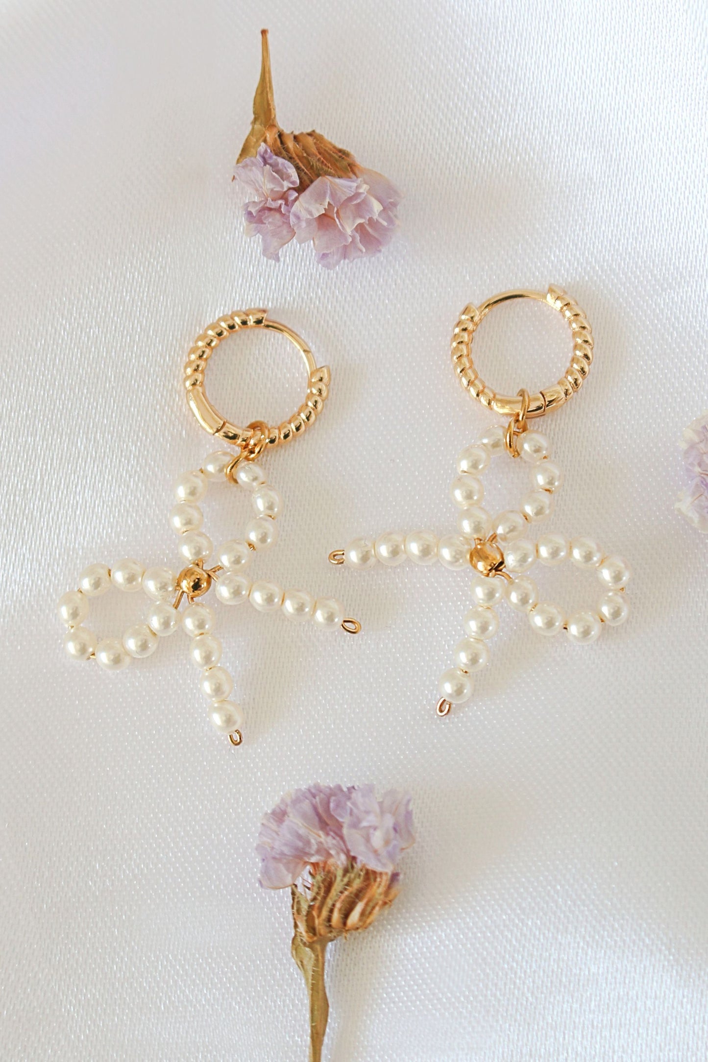 Gold and pearl earrings on a white background with dried flowers.