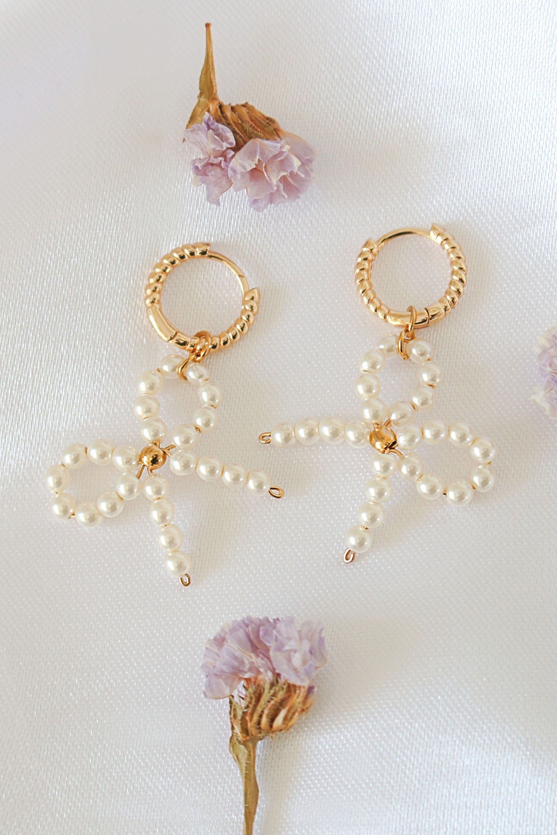 Gold and pearl earrings on a white background with dried flowers.