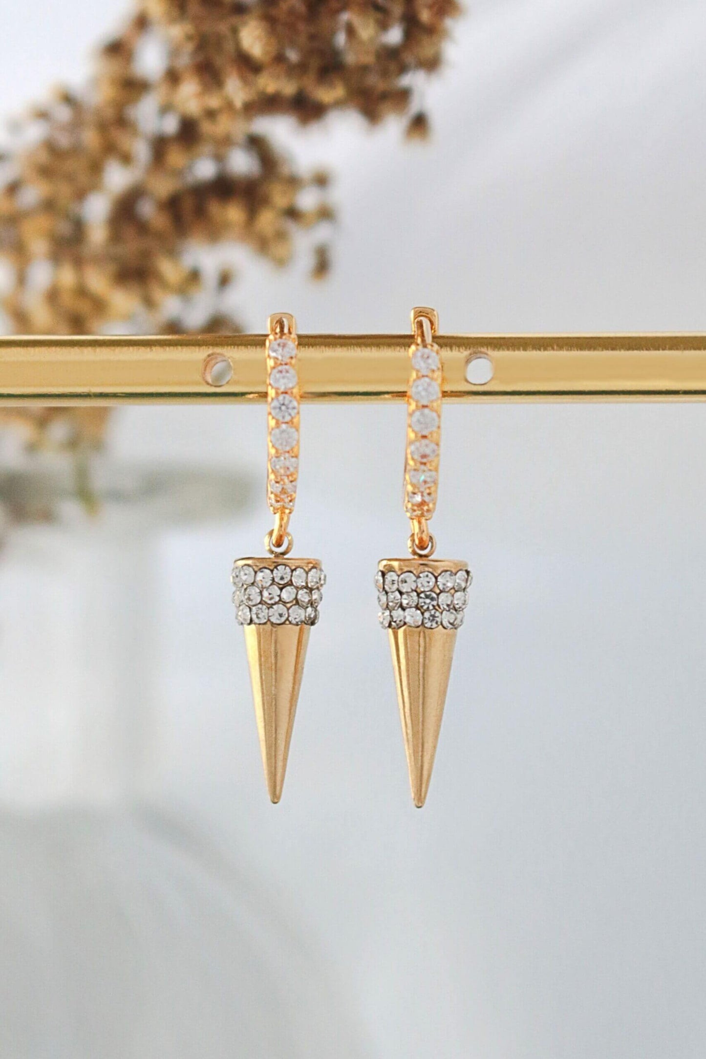 Gold spike earrings with clear gemstones on a gold stand against a blurred natural background