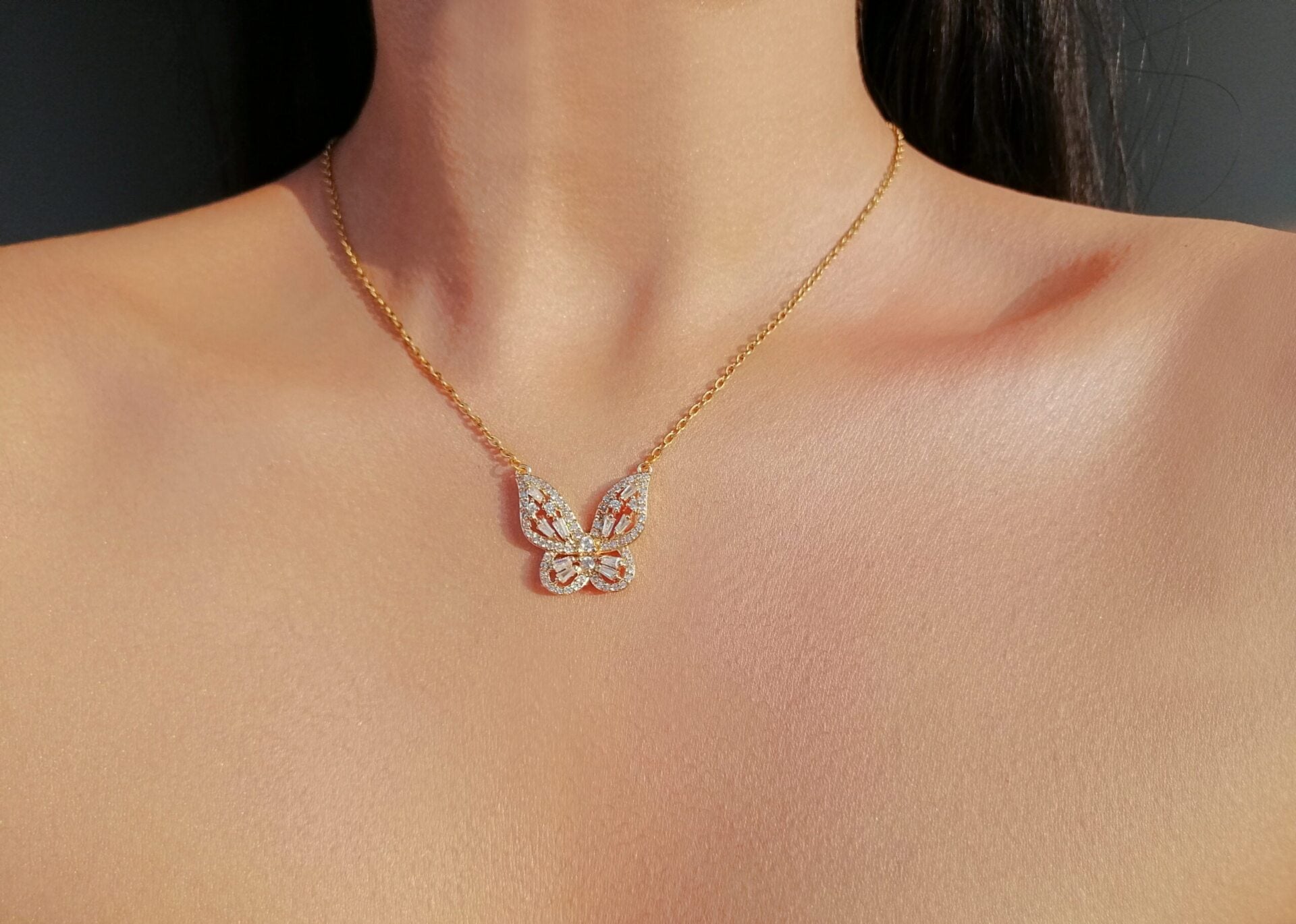 Gold necklace with a butterfly pendant on a person's neck against a dark background