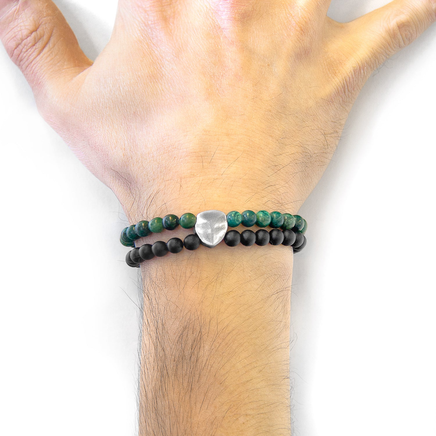 Hand wearing a bracelet with green and black beads and a silver heart charm on a white background