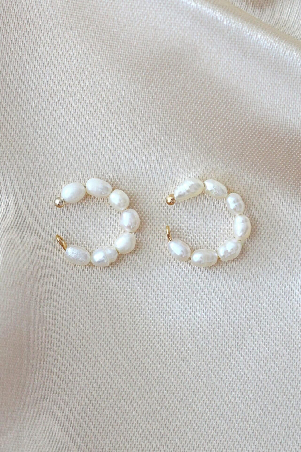 Pair of pearl hoop earrings on a light beige fabric background