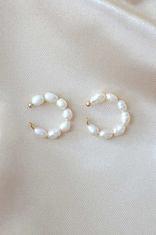 Pair of pearl hoop earrings on a light beige fabric background