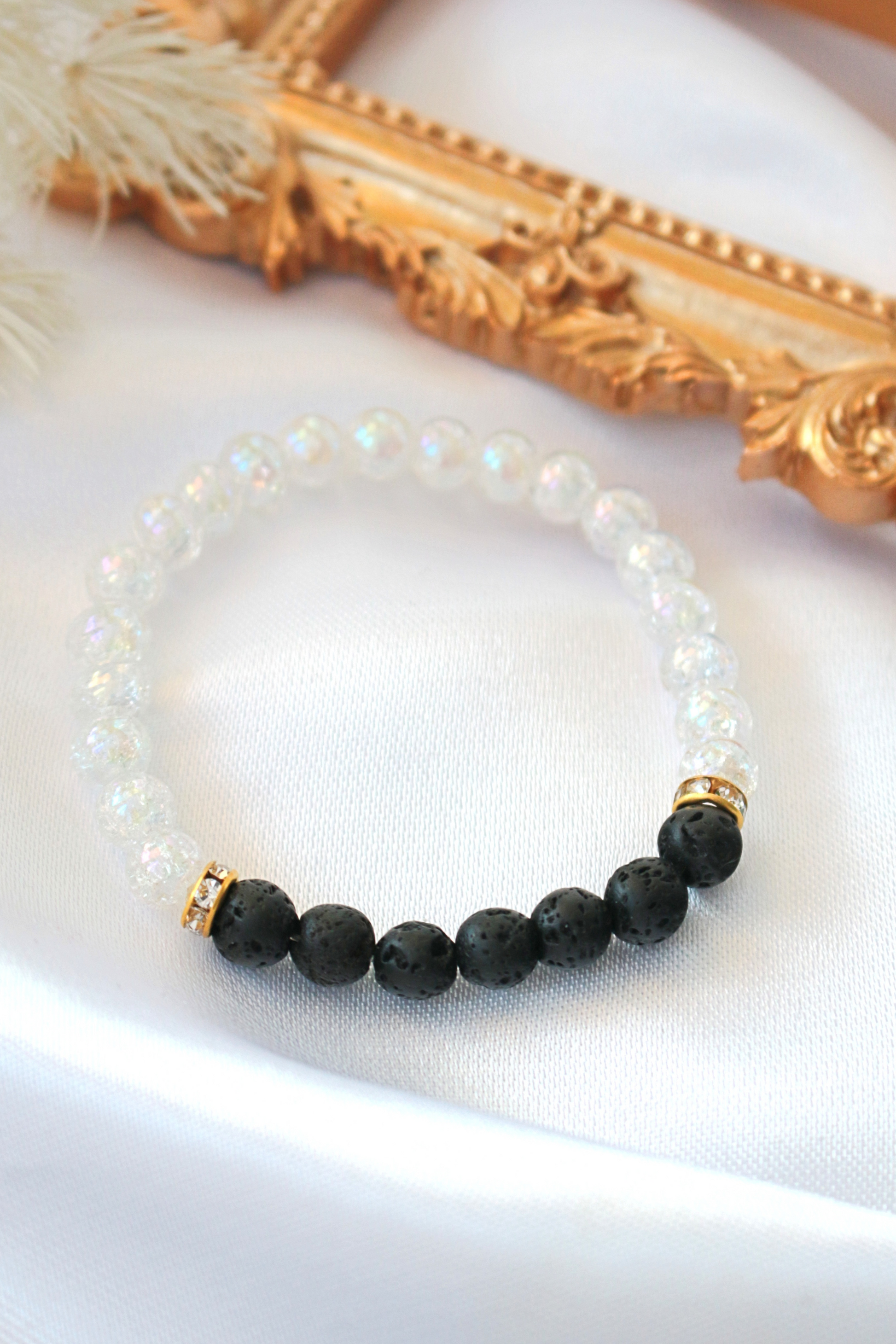 Bracelet with black beads and gold accents on a white surface with a decorative gold frame in the background.