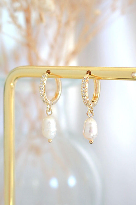 Gold hoop earrings with pearl drops on a gold stand against a soft, blurred background.