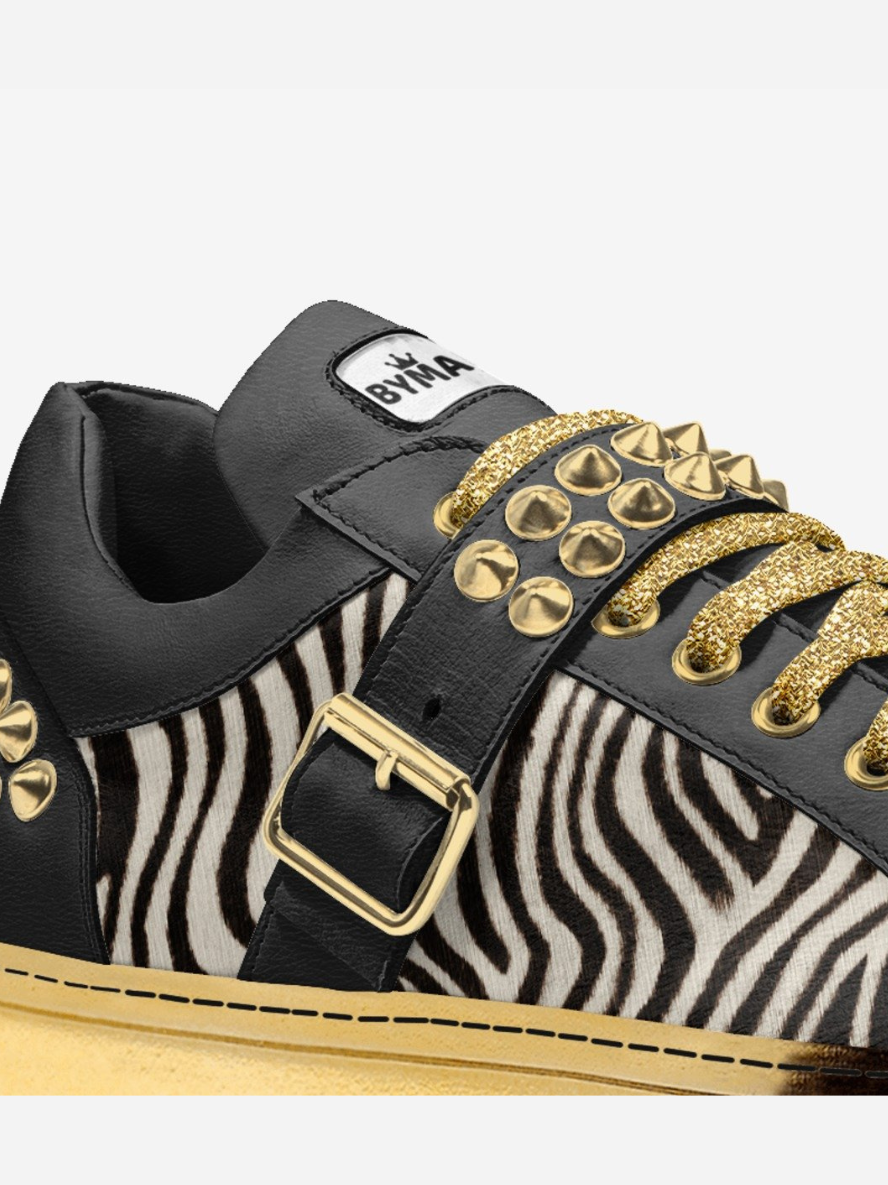 Black and gold sneaker with zebra pattern and gold studs on a white background