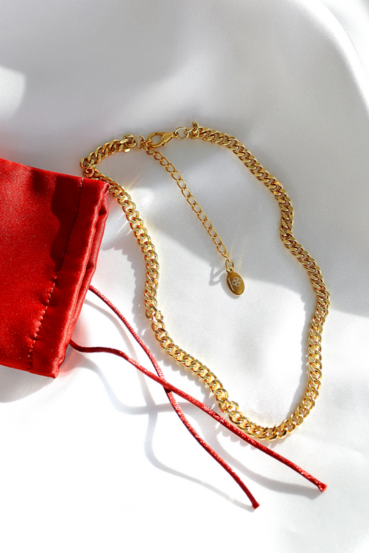 Gold chain necklace with a red fabric pouch on a white surface