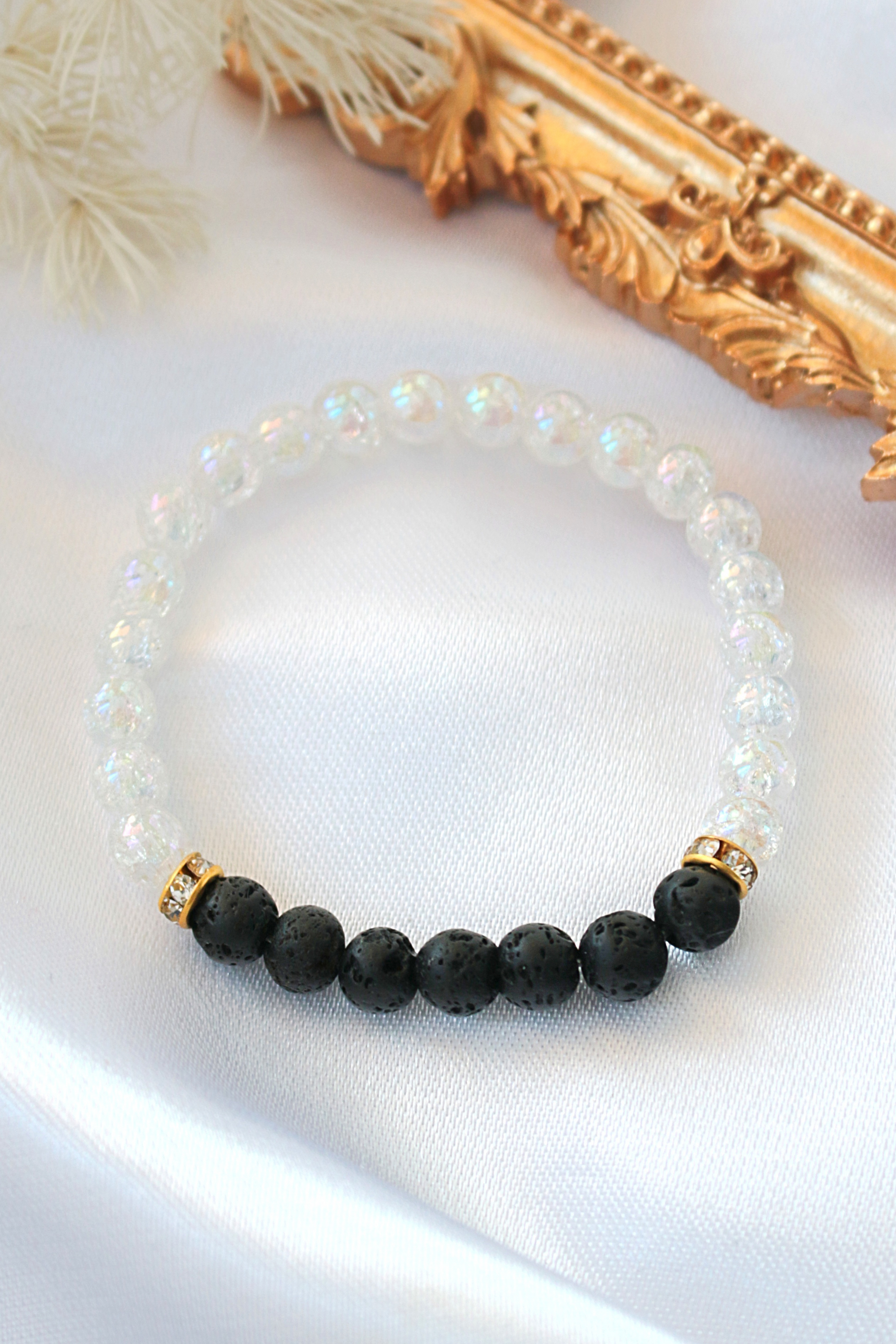 Bracelet with black beads and gold clasps on a white surface with a decorative gold frame in the background.