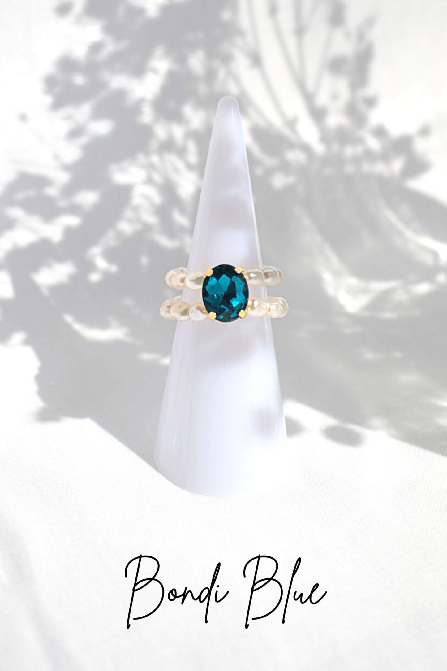 Gold ring with a blue gemstone on a white stand against a white background