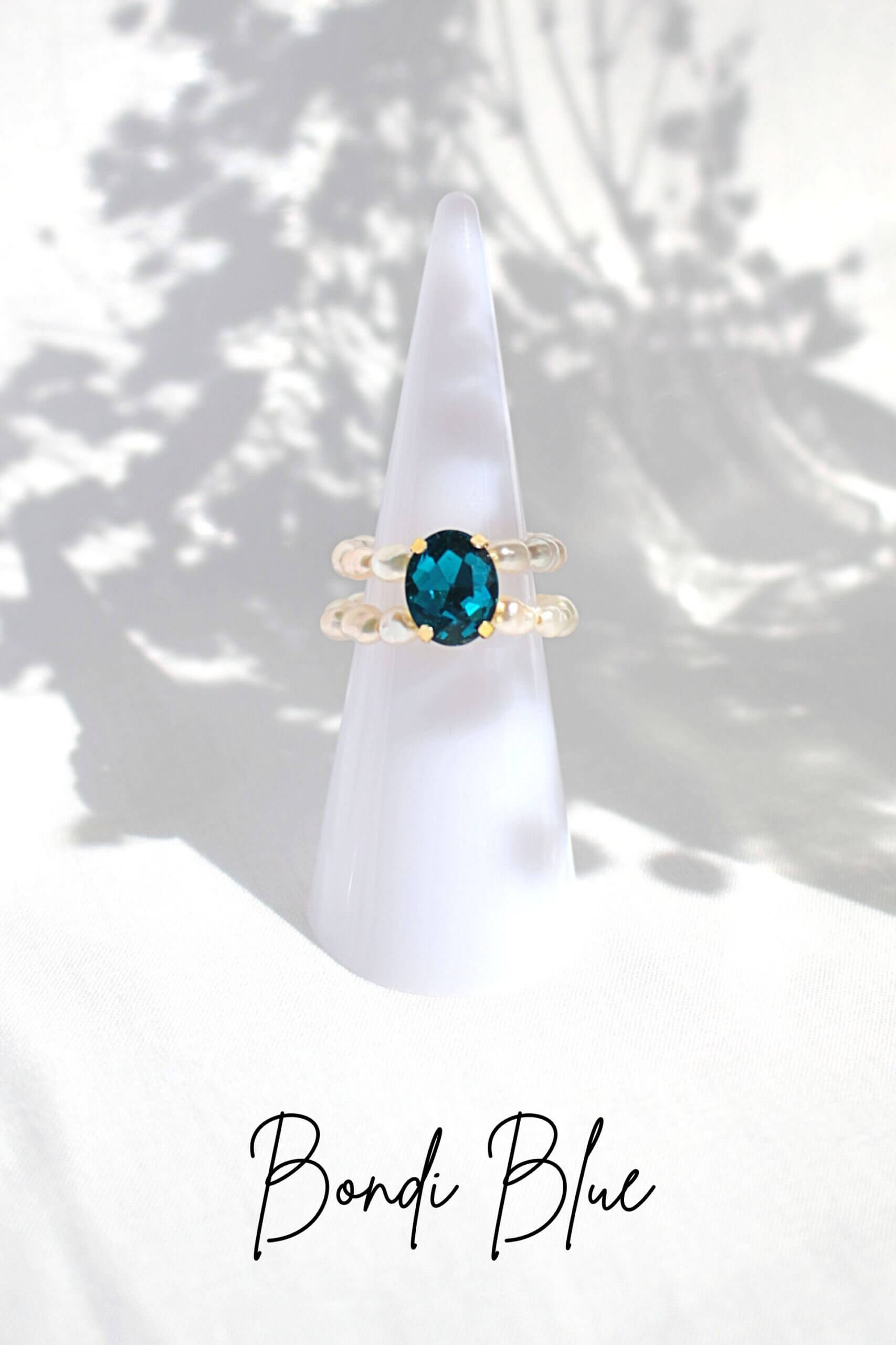 Gold ring with a blue gemstone on a white stand against a white background