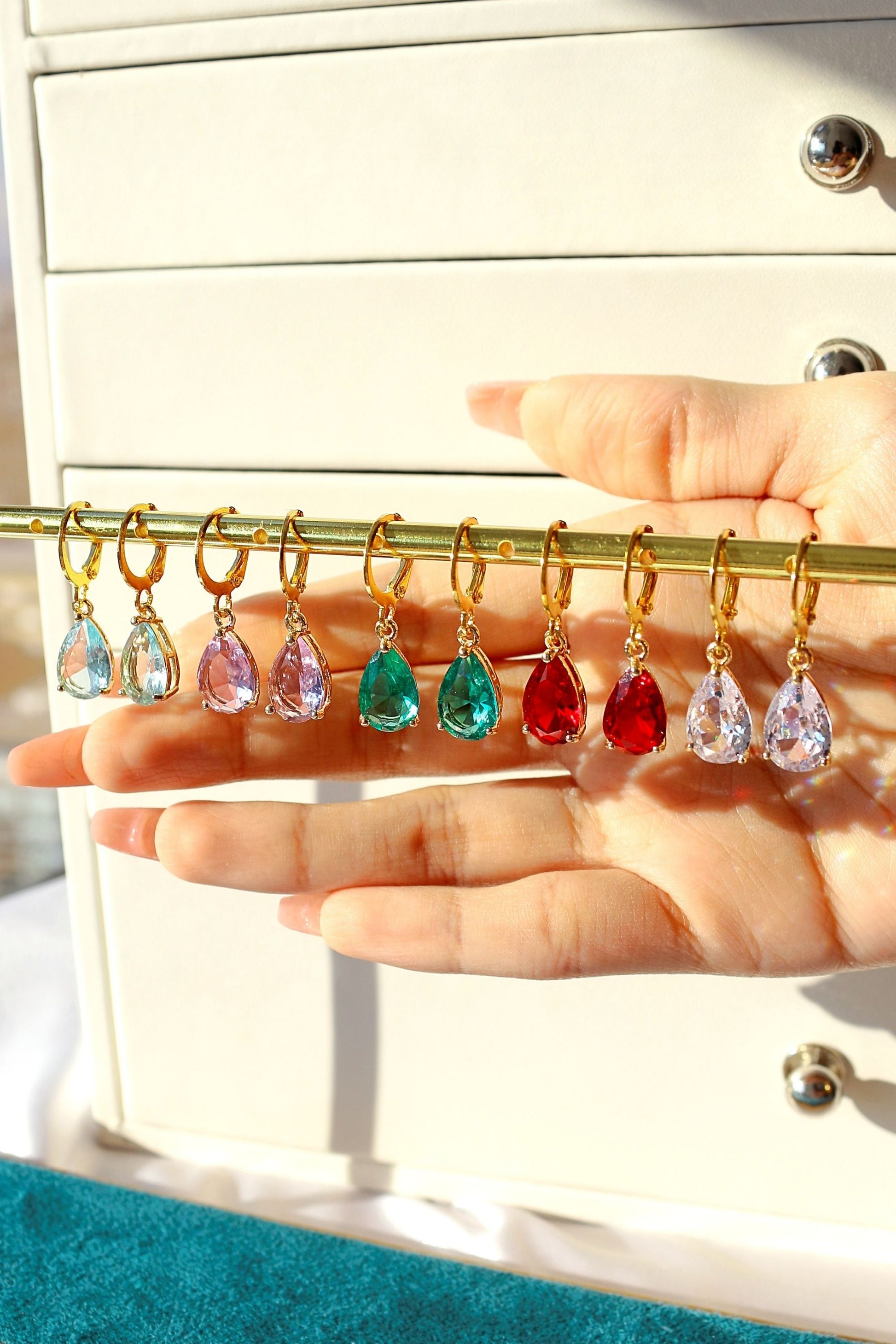 Colorful teardrop-shaped earrings on a gold earring stand held by a hand.