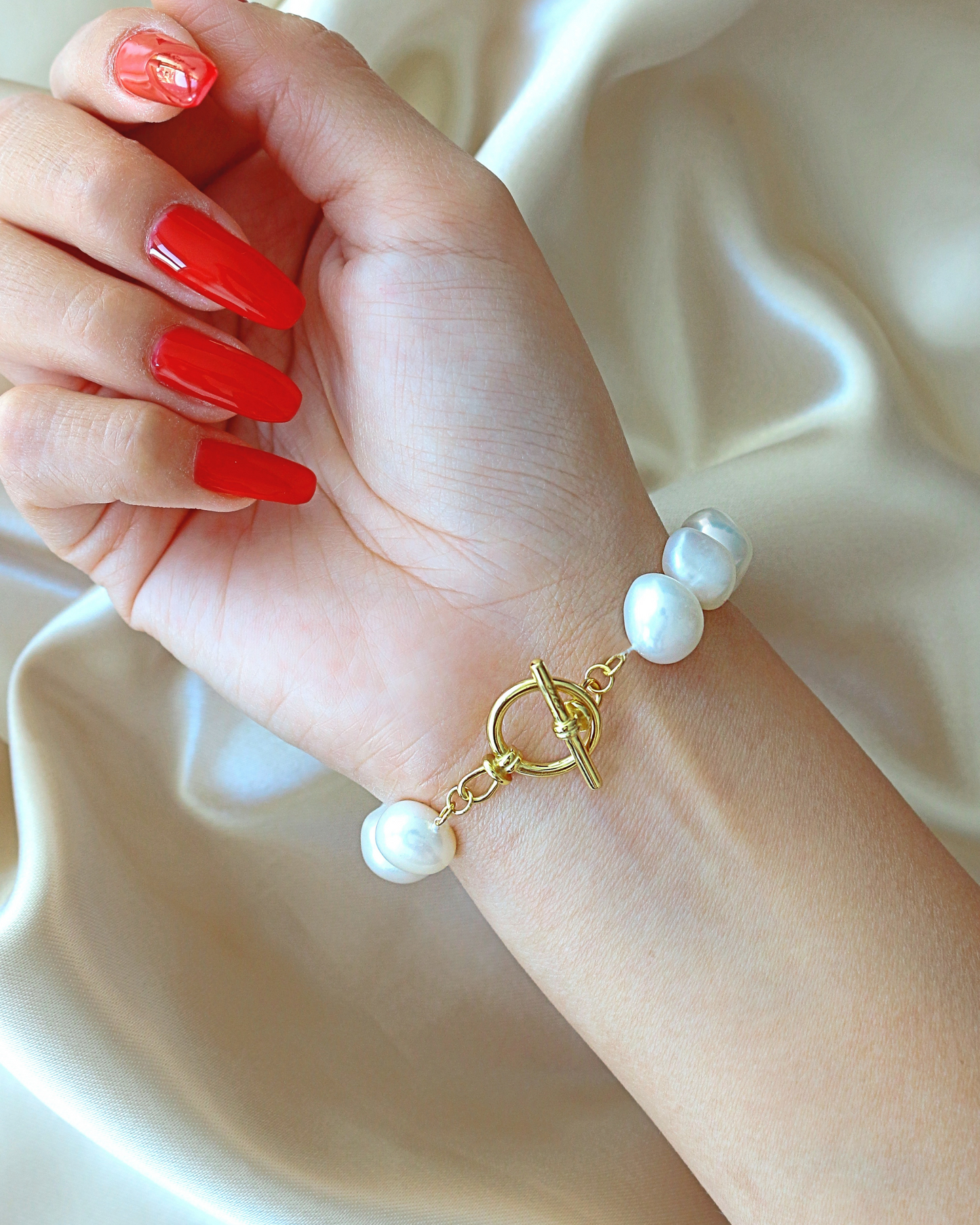 Hand wearing a pearl bracelet with red nail polish on a beige background