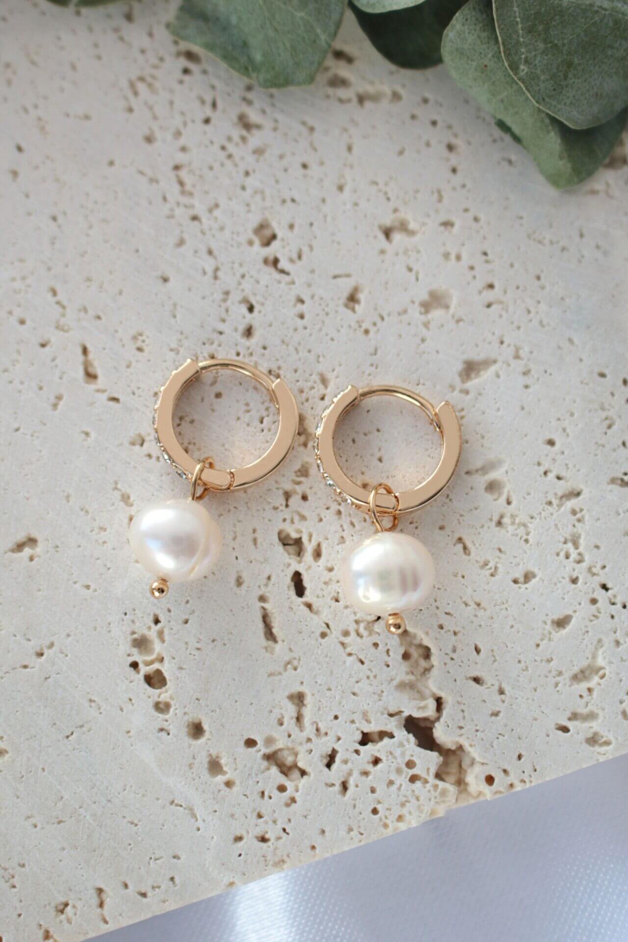 Gold hoop earrings with pearl drops on a textured surface