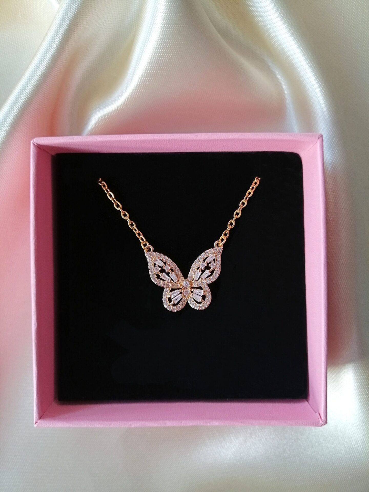 Butterfly necklace in a pink box on a white satin background