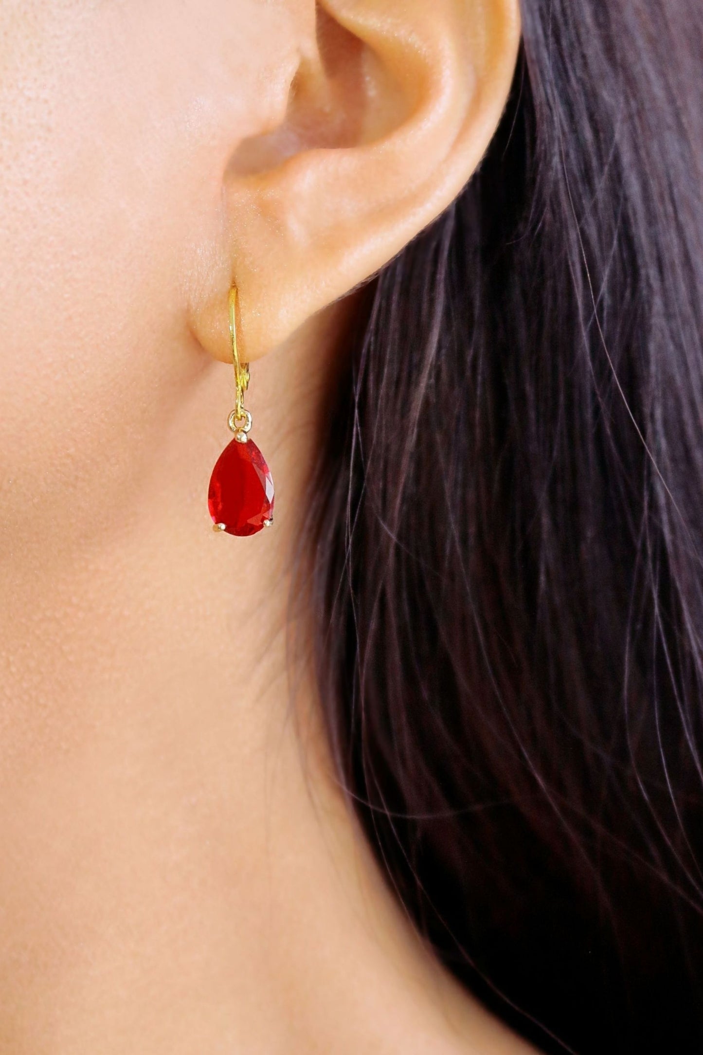 Close-up of a person wearing red teardrop earrings with gold hooks.