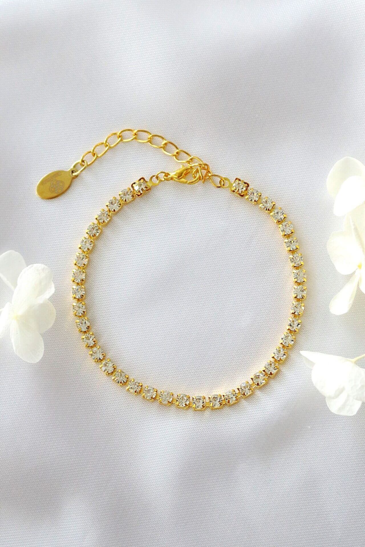 Gold bracelet with clear stones on a white background with flowers