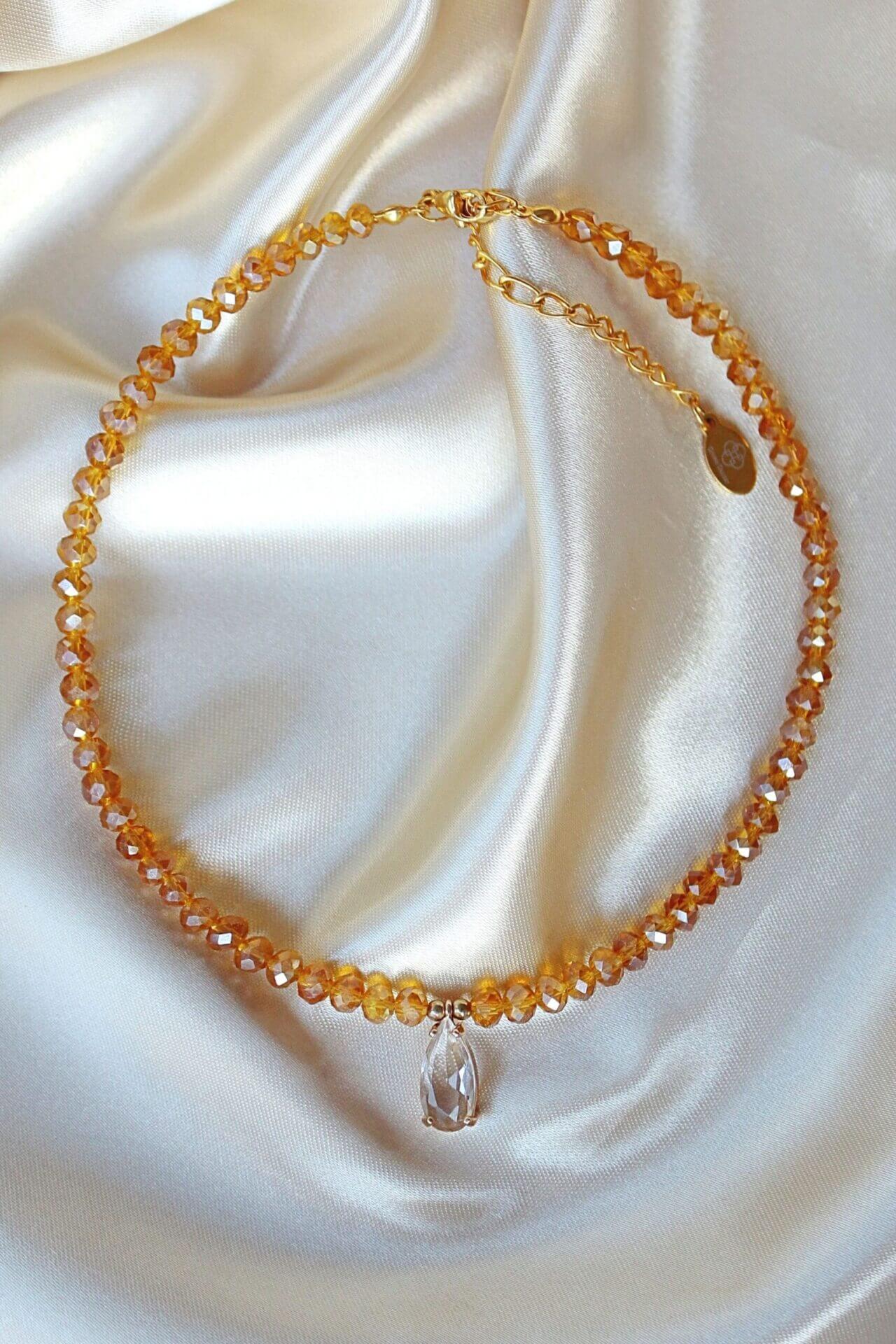 Necklace with orange beads and a clear crystal pendant on a white fabric background
