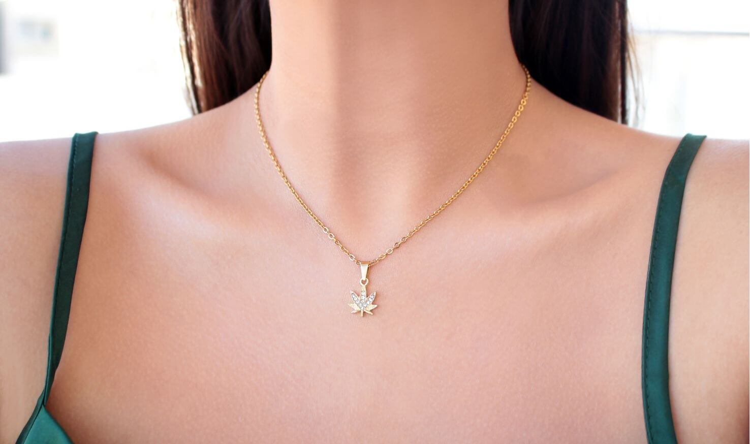 Gold necklace with a leaf pendant on a person wearing a green top.