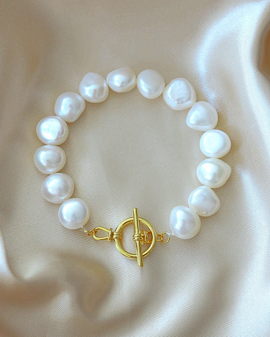 Pearl bracelet with a gold clasp on a beige fabric background