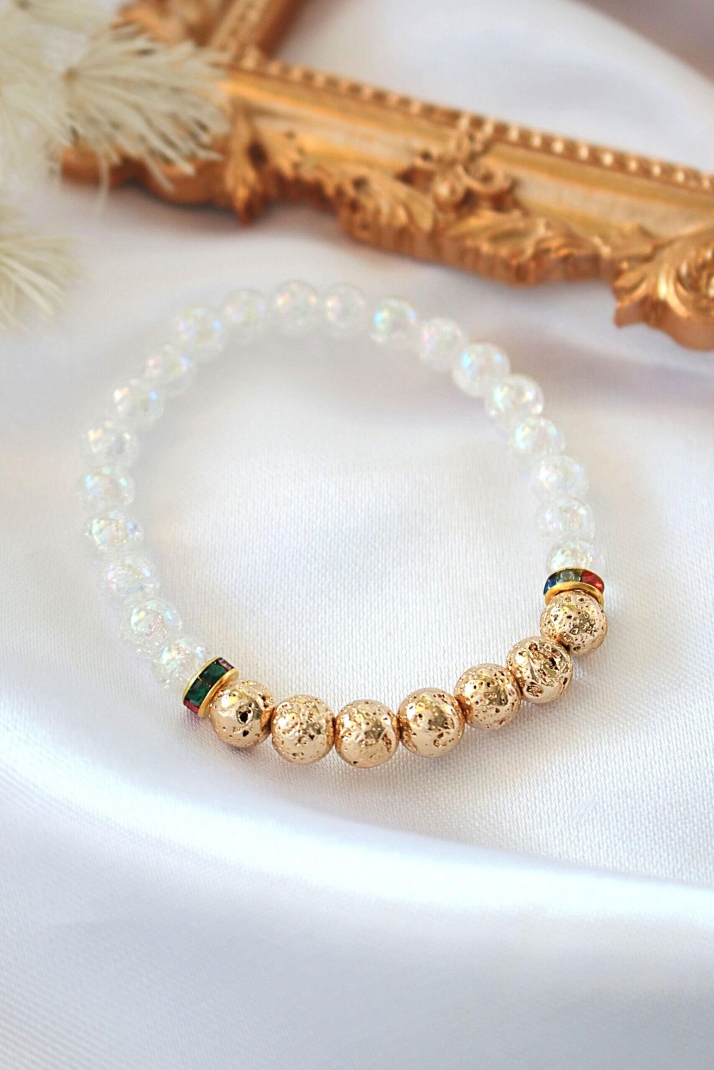Pearl and gold beaded bracelet on a white surface with a decorative gold frame in the background.