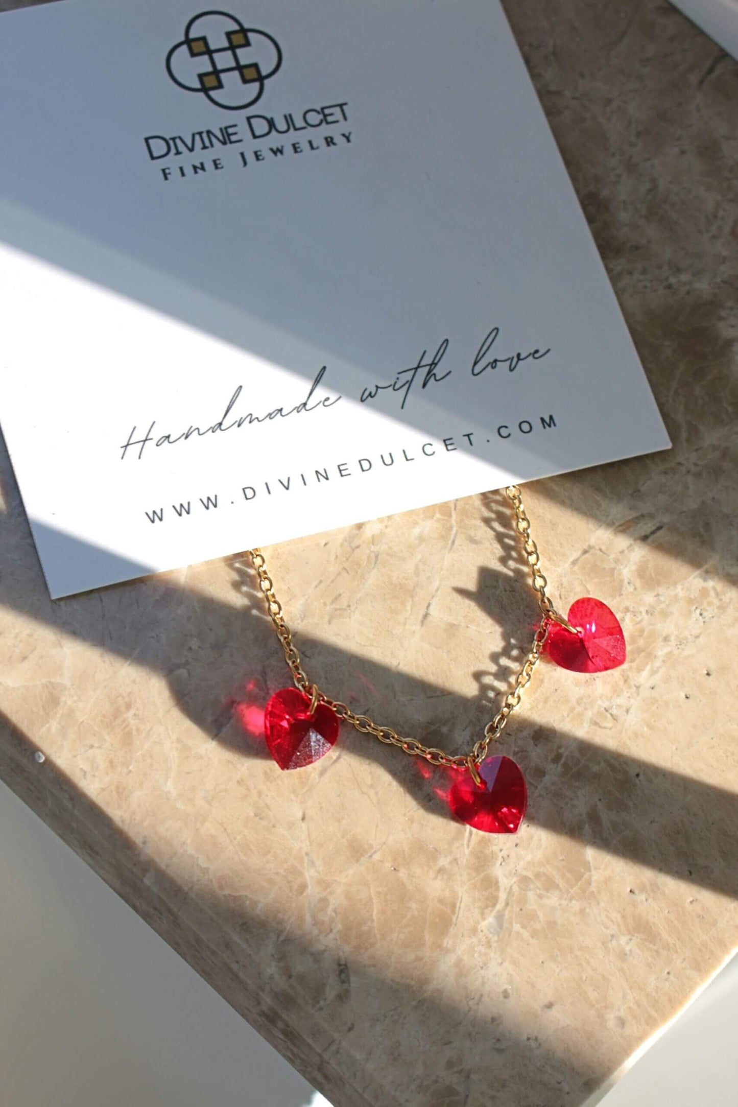 Gold necklace with red heart pendants on a Divine Dulcet card.