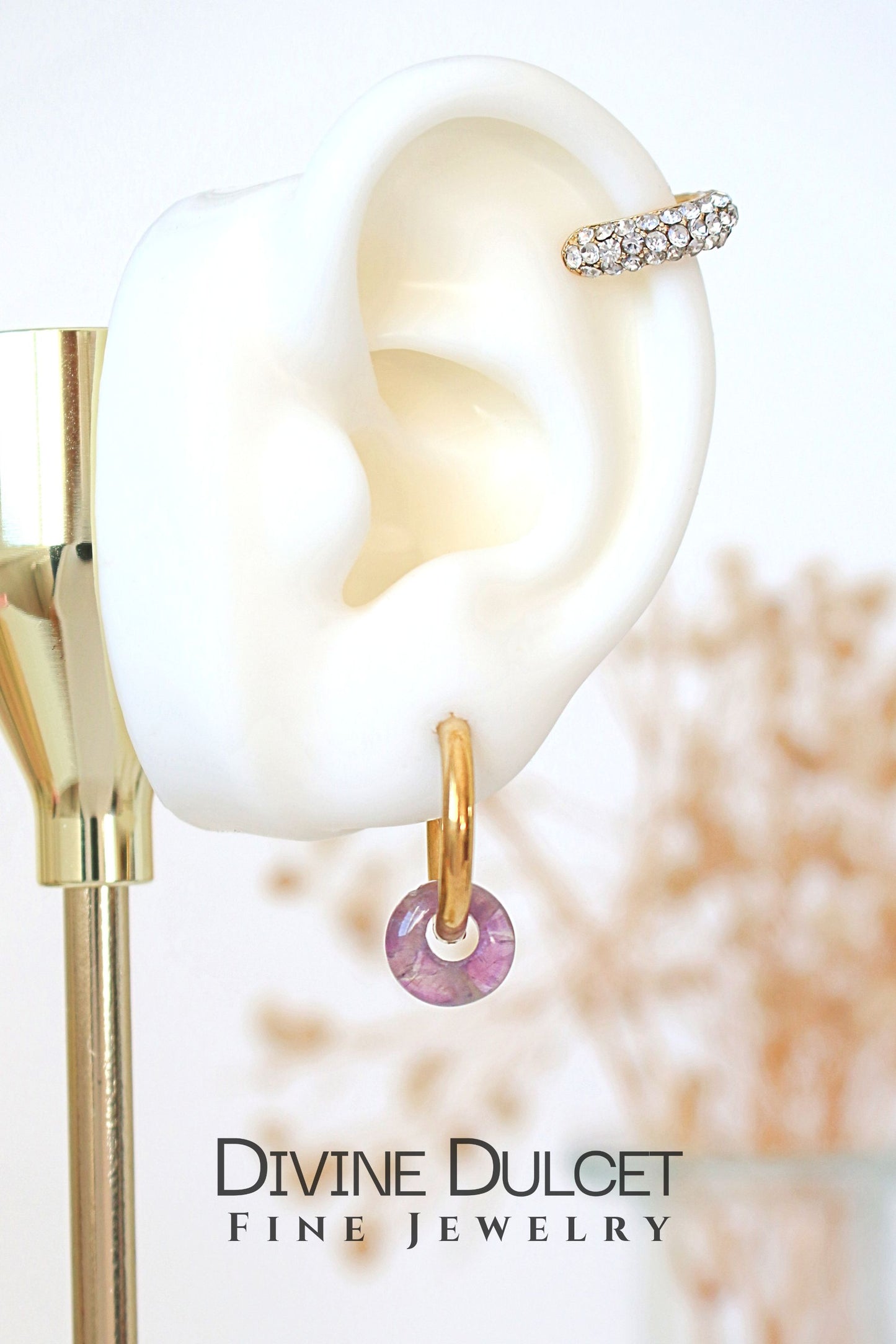 Gold and pearl earring with a blurred background, featuring 'Divine Dulcet Fine Jewelry'.