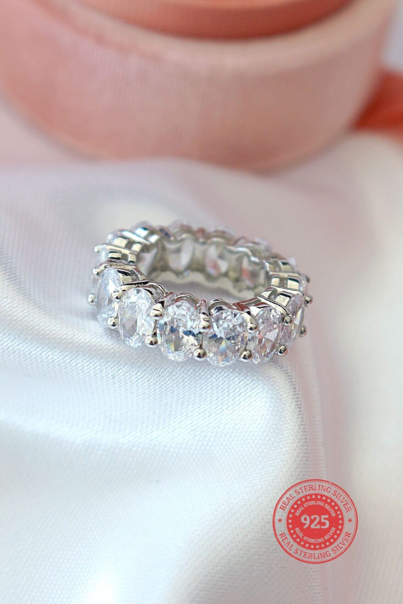 Silver ring with clear stones on a white fabric background, featuring a '925' stamp.