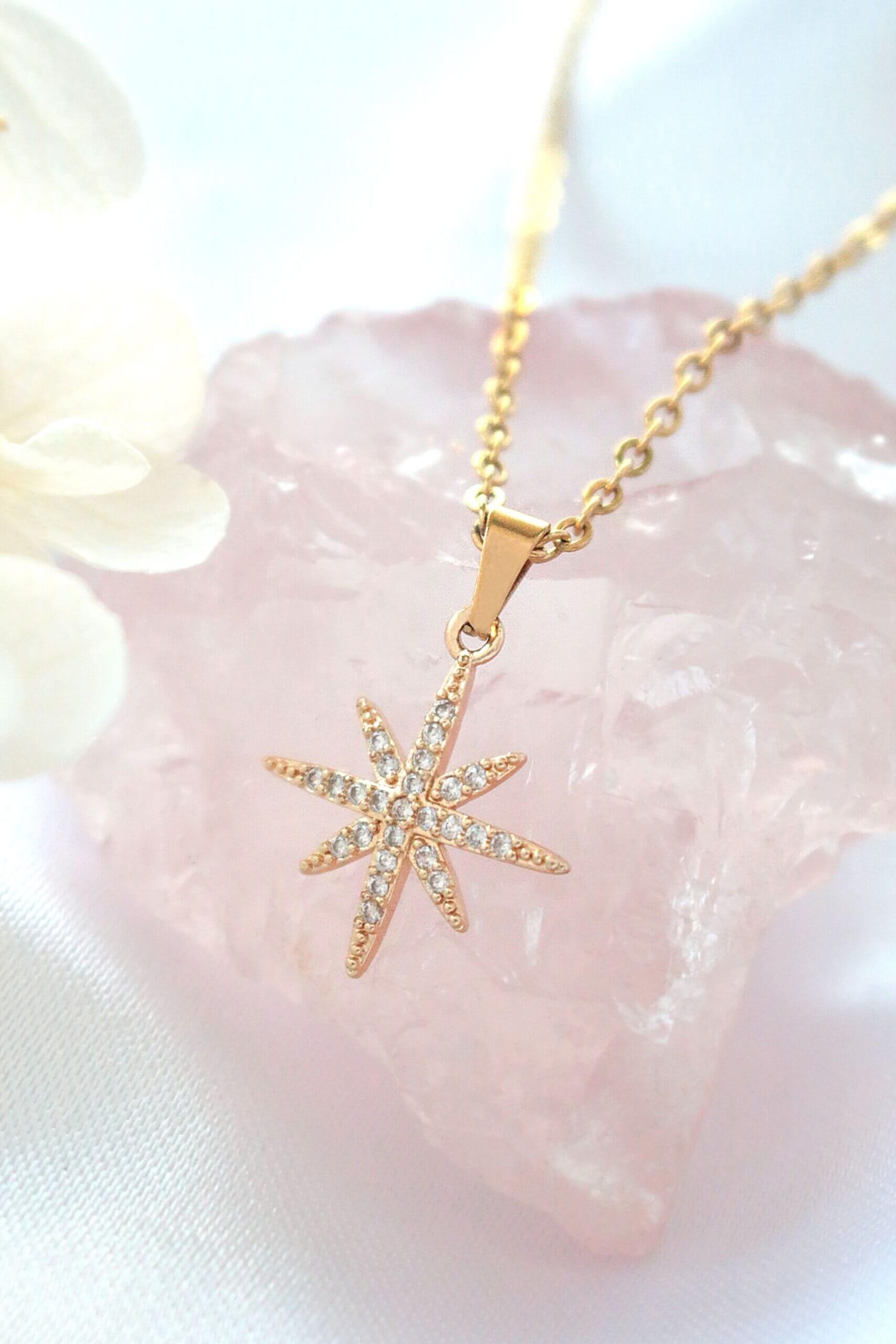 Gold star-shaped pendant necklace on a soft pink background