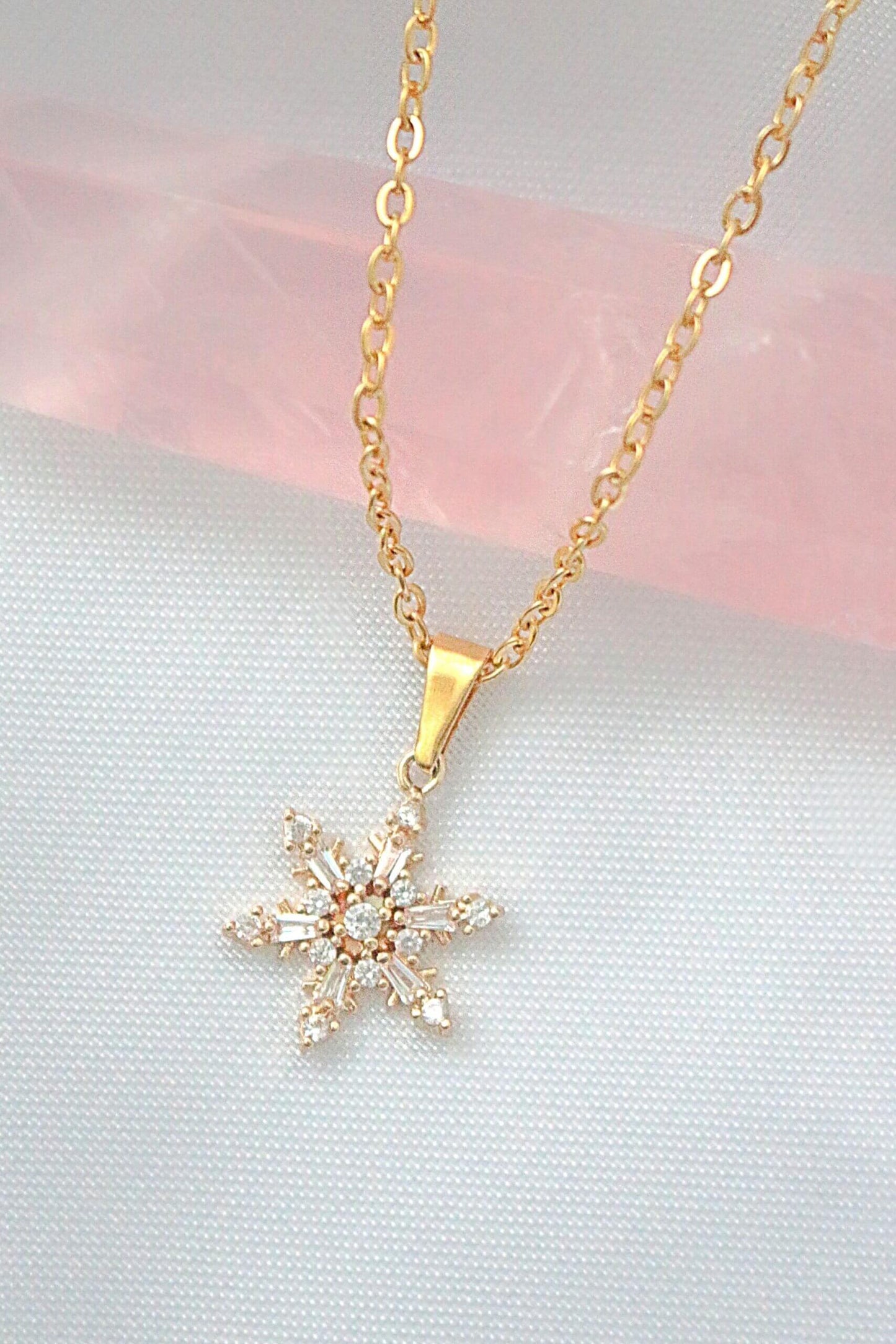 Gold snowflake pendant necklace on a soft pink and gray background