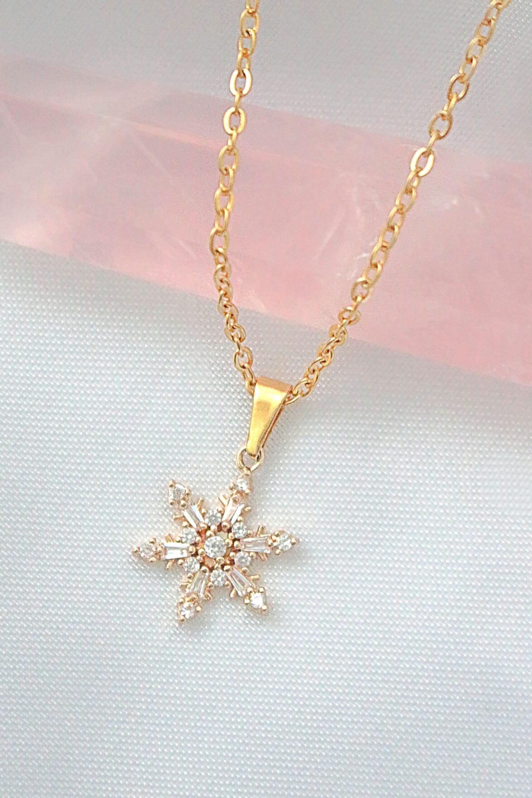 Gold snowflake pendant necklace on a soft pink and gray background