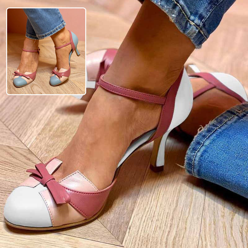 Close-up of a woman's feet wearing pink and white high-heeled shoes with a bow detail on a wooden floor.