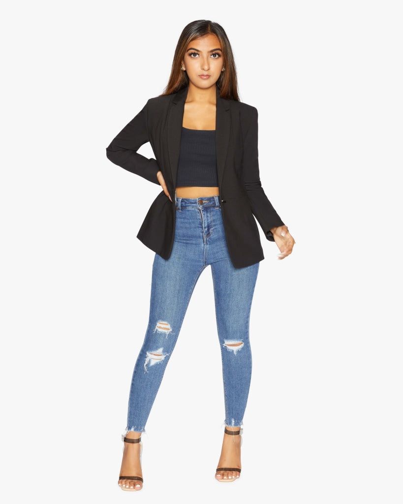 Woman wearing a black blazer, black top, and blue jeans on a white background