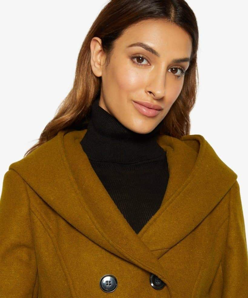 Woman wearing a mustard yellow coat with a black turtleneck underneath, on a white background.
