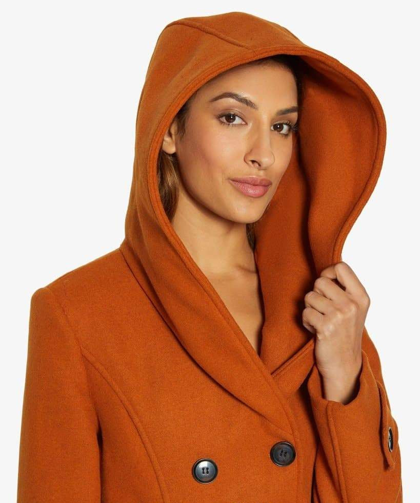 Woman wearing an orange hooded coat with a plain background