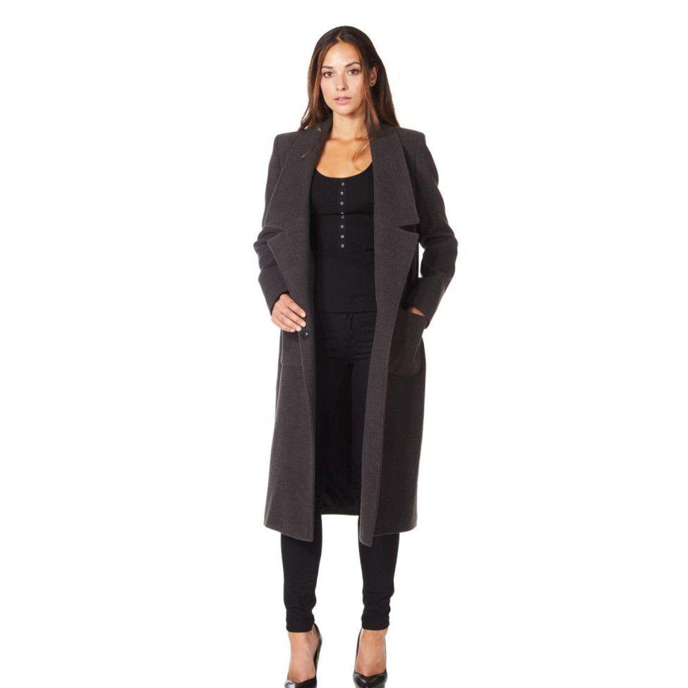 Woman wearing a long dark coat over a black outfit on a white background