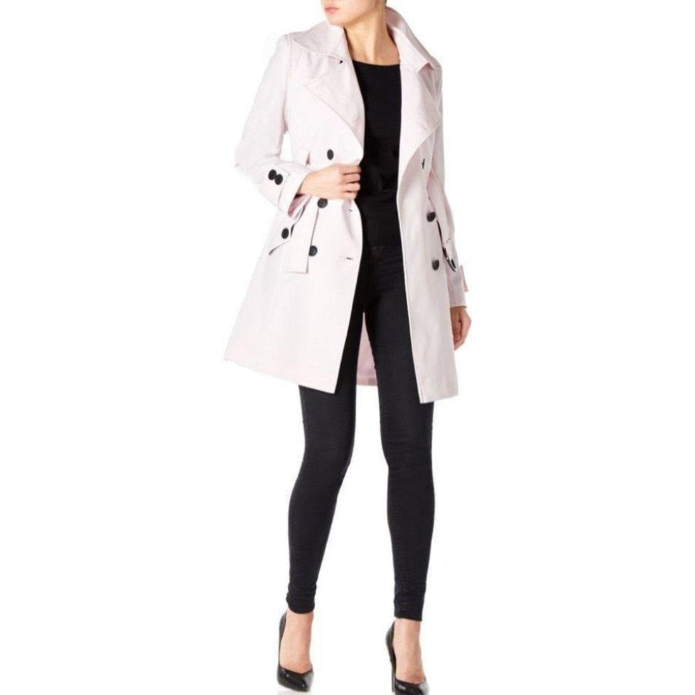 Woman wearing a light pink trench coat over a black outfit on a white background