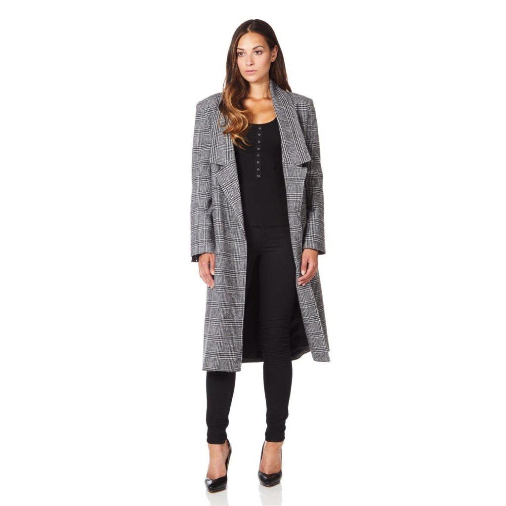 Woman wearing a long gray checkered coat over a black outfit on a white background