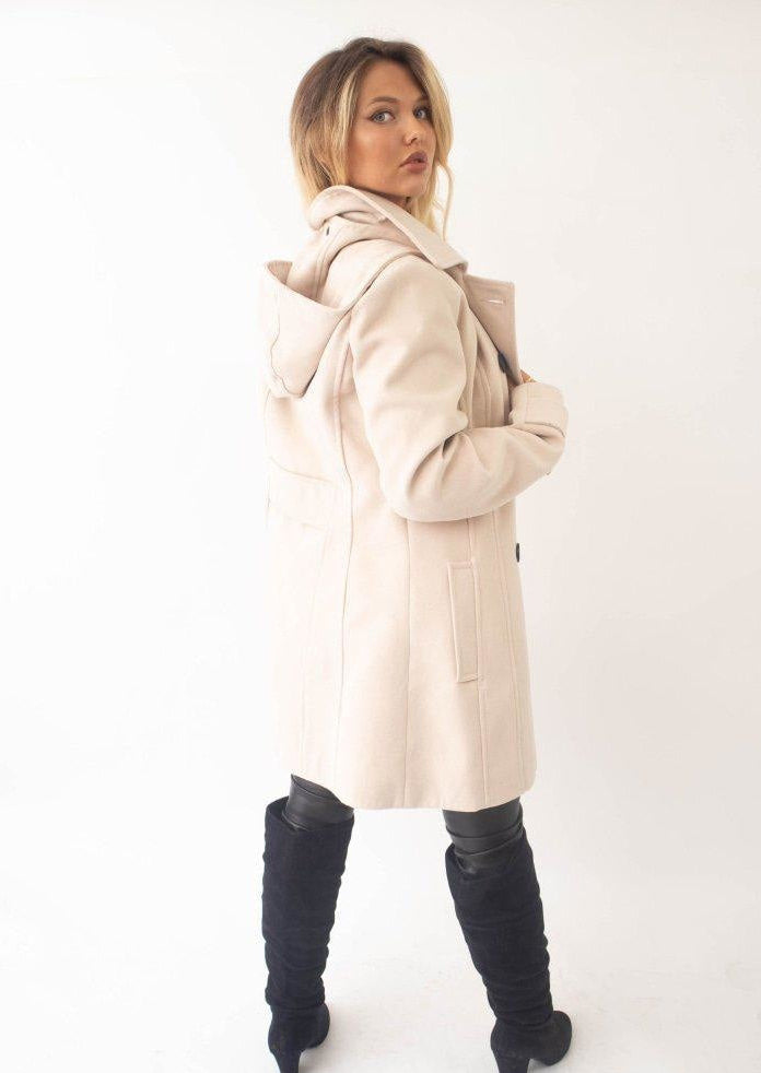 Woman wearing a beige coat and black knee-high boots on a white background