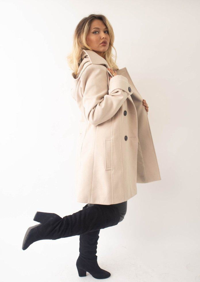 Woman wearing a beige coat and black boots on a white background