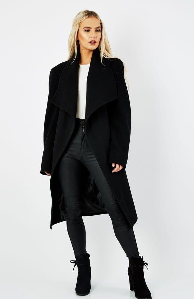 Person wearing a black coat, white shirt, black pants, and black boots on a white background.