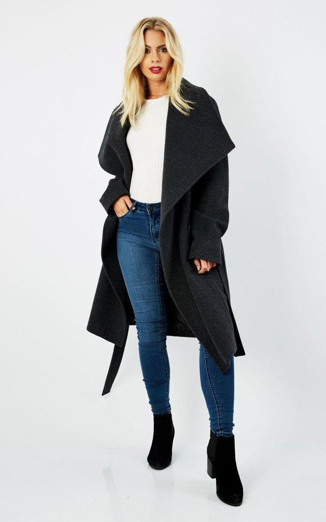 Woman wearing a black coat, white shirt, blue jeans, and black boots on a white background