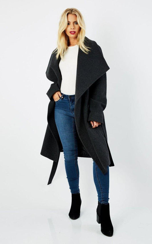 Woman wearing a black coat, white shirt, blue jeans, and black boots on a white background