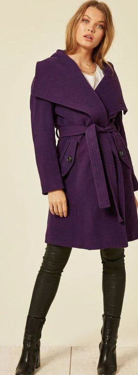 Woman wearing a purple coat with a belt, standing against a plain background.