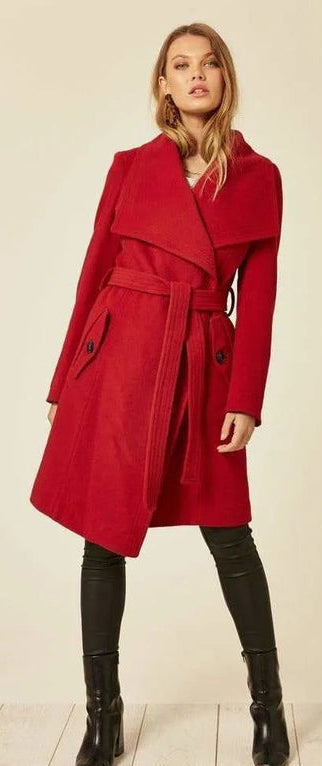 Woman wearing a red coat with a belt, standing against a plain background.