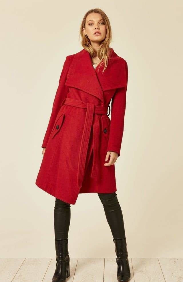 Woman wearing a red coat with a belt on a beige background